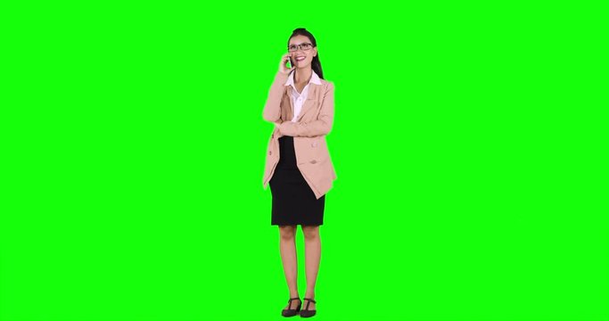 Full length of young Asian businesswoman makes a phone call while standing in the studio, shot in 4k resolution with green screen background