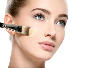 Girl applies  tonal foundation on face use makeup brush