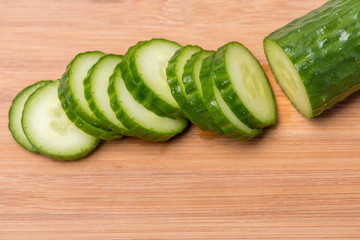 Ripe green cucumber cut in circles on a wooden board on a white background