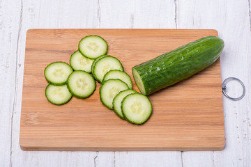 Ripe green cucumber cut in circles on a wooden board on a white background