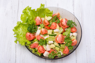 Delicious salad of vegetables, turnips, cucumber, tomato, avocado and parsley on a white background