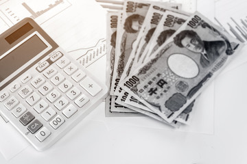 Calculator with blurred Japanese currency yen bank notes and coin on finance chart and graph...