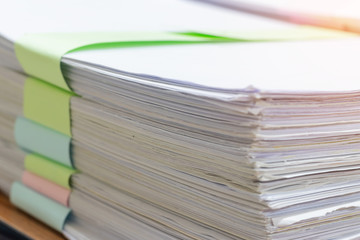 Close up pile of unfinished homework assignment stacked in archive with colorful papers on teacher's table waiting to be managed and inspected. Stack of paperwork. Education and business concept.