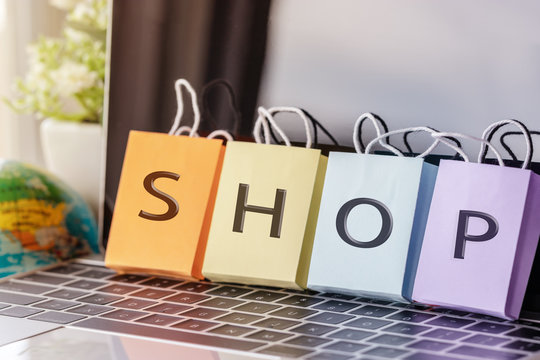Colorful shopping paper bag with shop text on laptop keyboard with globe nearby indoor on table. Consumer can buy product directly anywhere anytime from seller. Online shopping and e-commerce concept.