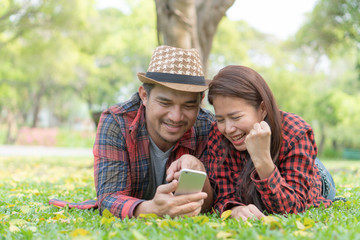 romantic couple dating in the park. lovers lying on the lawn looking at mobile phone together.