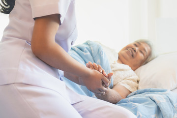 asian female home nursing holding hand of older lady on the bed and encouraging patient
