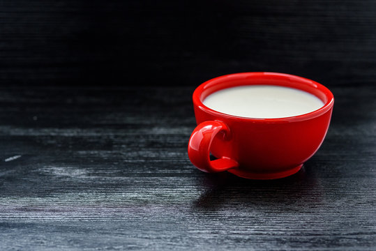 Milk in a red mug on a black wooden background