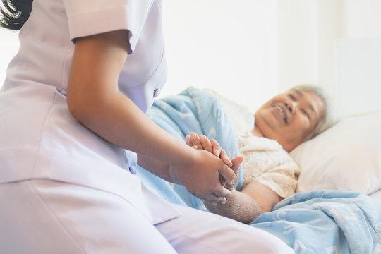 Asian Female Home Nursing Holding Hand Of Older Lady On The Bed And Encouraging Patient