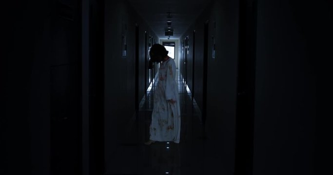 Horrible creepy zombie woman walking in the dark hospital corridor at night. Shot in 4k resolution