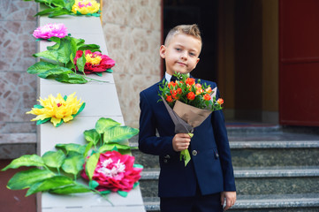 Beautiful boy in a bouquet of flowers . A first grader holding a flowers.  Fashionable boy in a suit