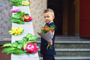 Beautiful boy in a bouquet of flowers . A first grader holding a flowers.  Fashionable boy in a suit