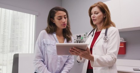 Mid aged medical doctor using portable tablet to review test results of patient - Powered by Adobe
