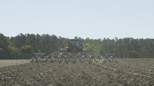 Green tractor tilling and pulling up dirt in a field with an implement
