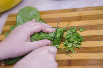 Woman cutting sorrel by knife on the wooden cooking desk