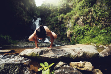 Young woman doing yoga near waterfall in tropical forest