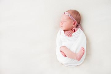 Cute newborn baby lies swaddled in a white blanket. Copy space and top view - obrazy, fototapety, plakaty