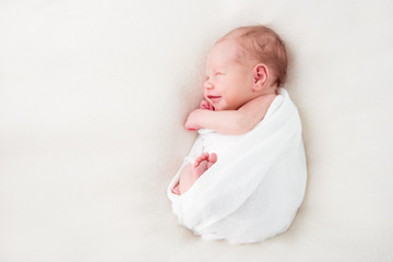 Smiling newborn baby sleeps swaddled in a white diaper