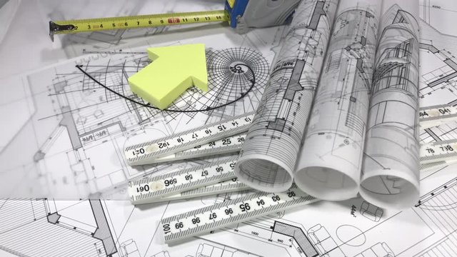 Blueprints - rolls of architectural drawings, roulette, yardstick - folding ruler and house symbol from a pack of yellow stickers smoothly rotate on the surface of the architectural drawings