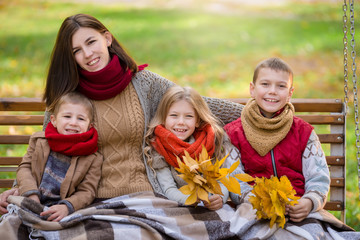 Family autumn look. Mother and three children ride on a swing in the autumn park