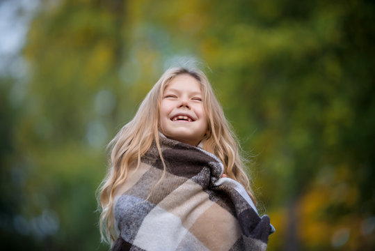 Portrarait of positive little girl covered in plaid in the autumn park