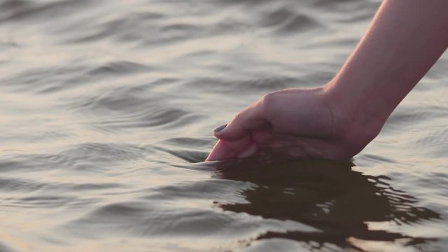 Slow motion closeup young female hand touches water waves at sunset