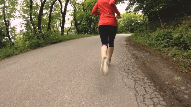 Running girl. Blonde girl doing outdoor sports in the summer forest. Rear view slow-motion wide angle. Close-up of a girl's legs