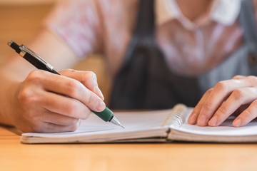 Woman hand writing in notebook on wooden table