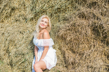 Nature time vacation and people concept - young woman dreaming on cereal field. . Beauty romantic girl outdoors against hay stack. Photo of sexy blonde in a field with haystacks 