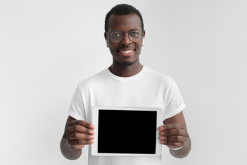 Daylight shot of african american man isolated on gray background in white t-shirt, holding tablet...