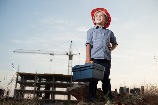 cute little kid in builder helmet with toolbox in hand on construction site