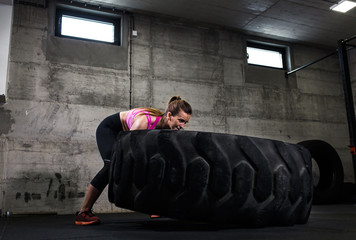 Fitness woman flipping wheel tire in the gym.