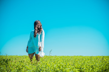 Naklejka na ściany i meble Freedom concept. Young happy woman in green field, evening light. Blue sky behind. Beauty Girl Outdoors enjoying nature. Beautiful Teenage Model girl in white dress running on the meadow 