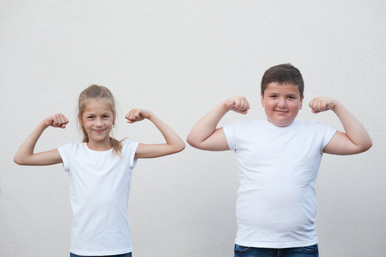 two children little thin girl and thick boy showing their muscle copyspace