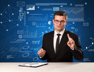 Young handsome businessman sitting at a desk with blue charts and data behind him