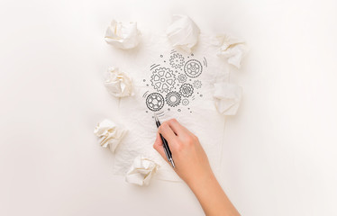Female hand next to a few crumpled paper balls drawing rotating gears