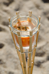 detail of decorative orange candle in glass jar in wooden holder with sandy background, outdoor on the beach