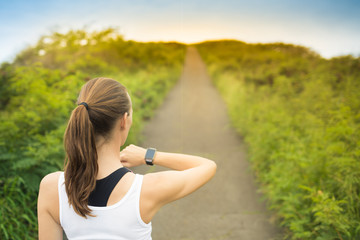 Female rummer looking at smart watch before run. Fitness technology concepts. 
