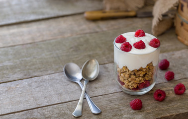 Yogurt with muesli in glass bowl with pieces raspberries on top.