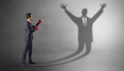 Fototapeta premium Businessman with boxing gloves fighting with disarmed businessman shadow 
