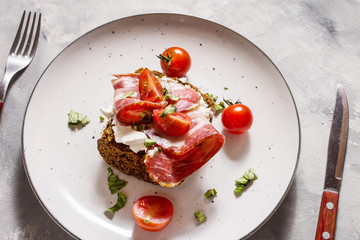 Sandwich with cherry tomatoes and prosciutto on plate over concrete background