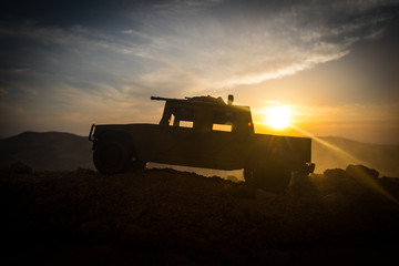 Fototapeta premium Military patrol car on sunset background. Army war concept. Silhouette of armored vehicle with gun in action. Decorated.