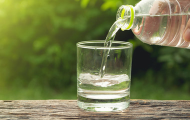 Female hand pouring water from bottle to glass on nature background.