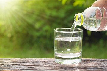 Female hand pouring water from bottle to glass on nature background.