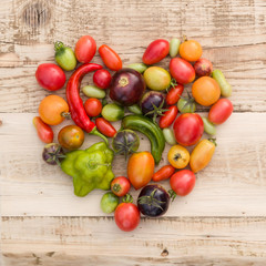 Closeup of colorful organic vegetables: tomatoes and paprika in the shape of a heart on old wooden background. Healthy food concept.