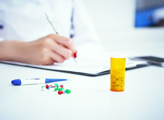 Pills and electronic thermometer laying on the table with female medicine doctor working on background. Medicine doctor prescribes medicine to the patient. Healthcare and medical concept.
