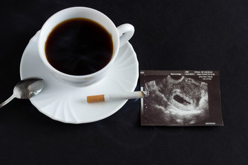 A cup of coffee and a burning cigarette, next to it there is a photograph of the uzi of pregnancy, pregnancy and smoking, pregnancy