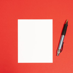 an empty white sheet and a pen on a red surface