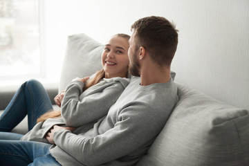 Loving young couple hugging relaxing on cozy sofa at home, smiling boyfriend and girlfriend looking in eyes enjoying each other company resting on couch, lovers embrace spending time together at home