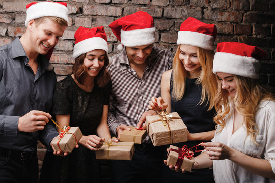 Christmas party, New Year celebration, sale, black friday, holiday, fun, togetherness. Group of happy smiling people in Santa caps opening gift boxes