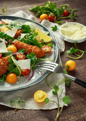 Fresh salad with chicken nuggets, cherry tomatoes, goat cheese and green vegetables in a rustic wooden table